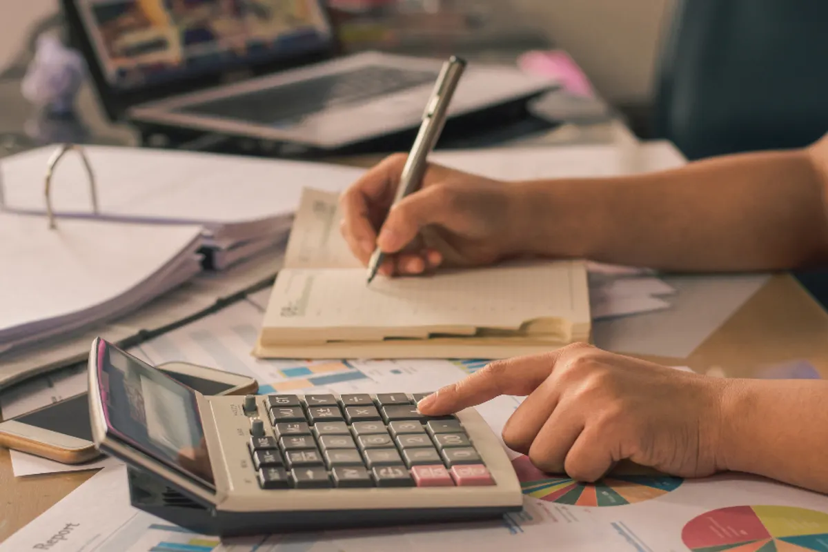 Hands working out figures on a calculator beside paperwork and a calendar