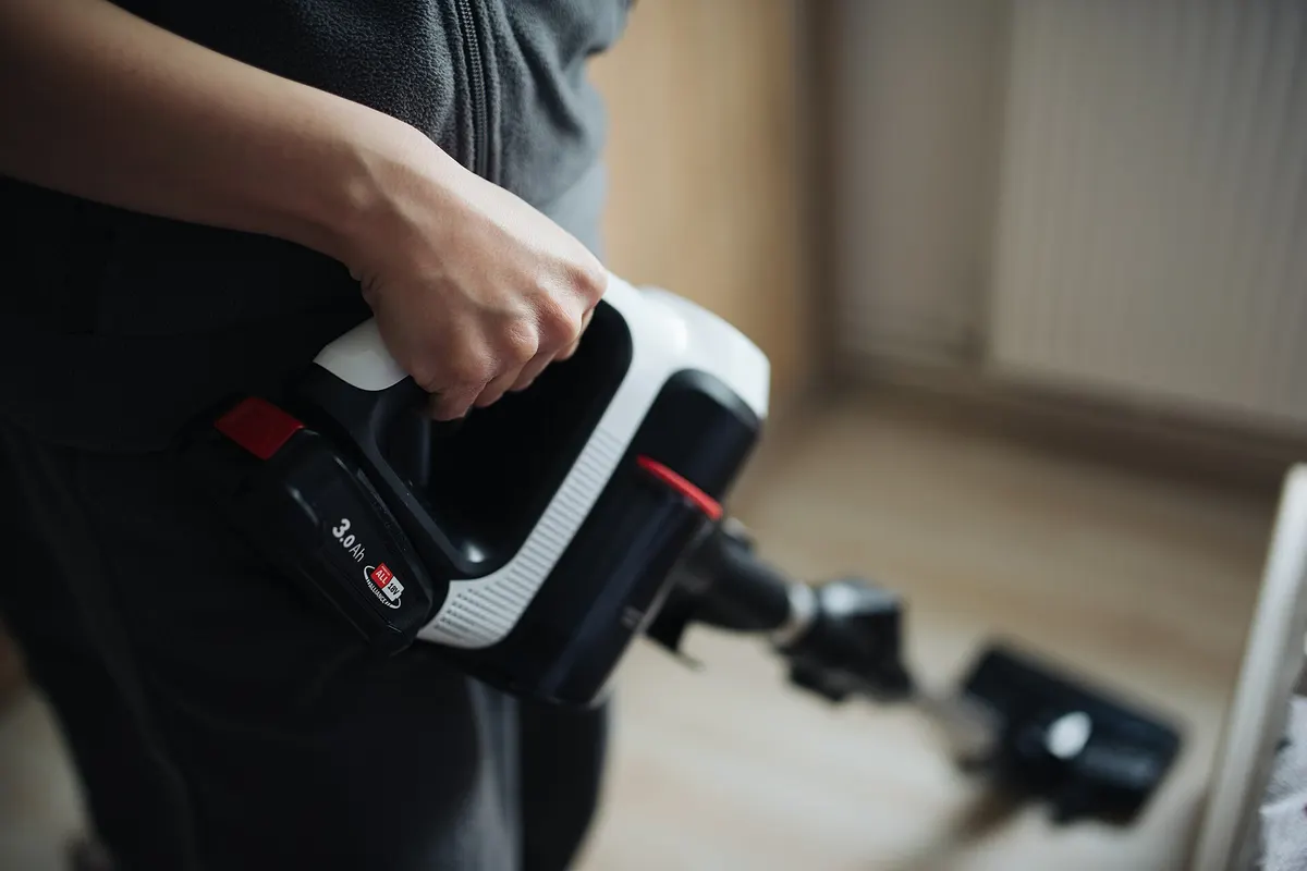A hand holding a white cordless vacuum cleaner over a wooden floor