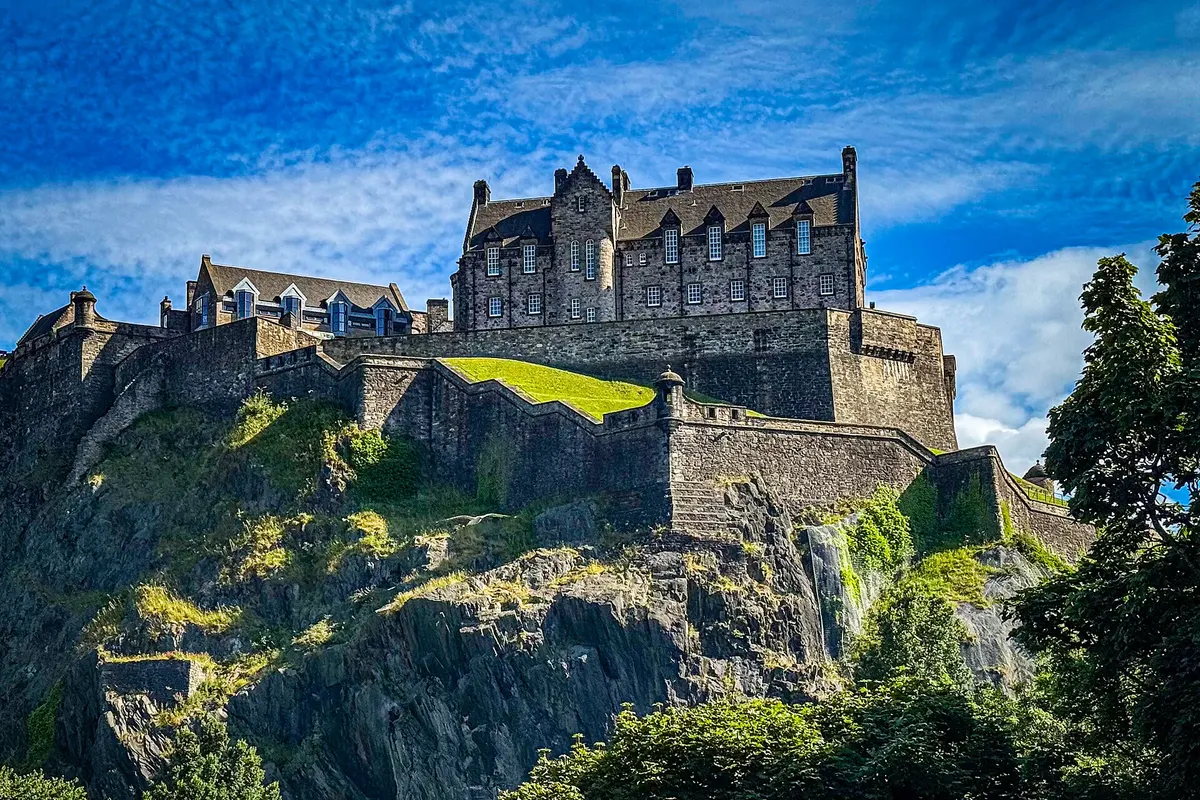 Edinburgh Castle on its volcanic rock above green trees under a bright blue sky