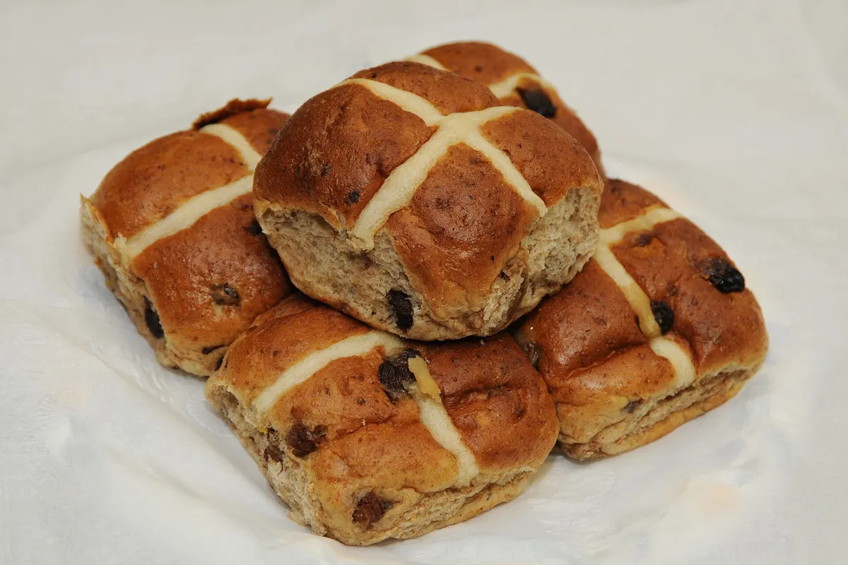 Glazed hot cross buns with raisins piled on a white cloth