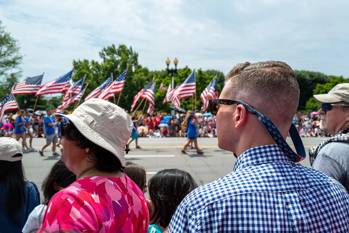 Spectators watching marchers carry American flags in the National Independence Day Parade in Washington, D.C.
