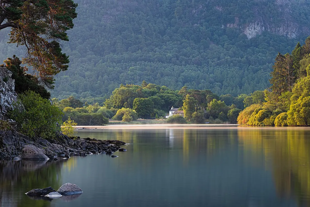 Still water and wooded shore at Friar’s Crag on Derwentwater in the Lake District