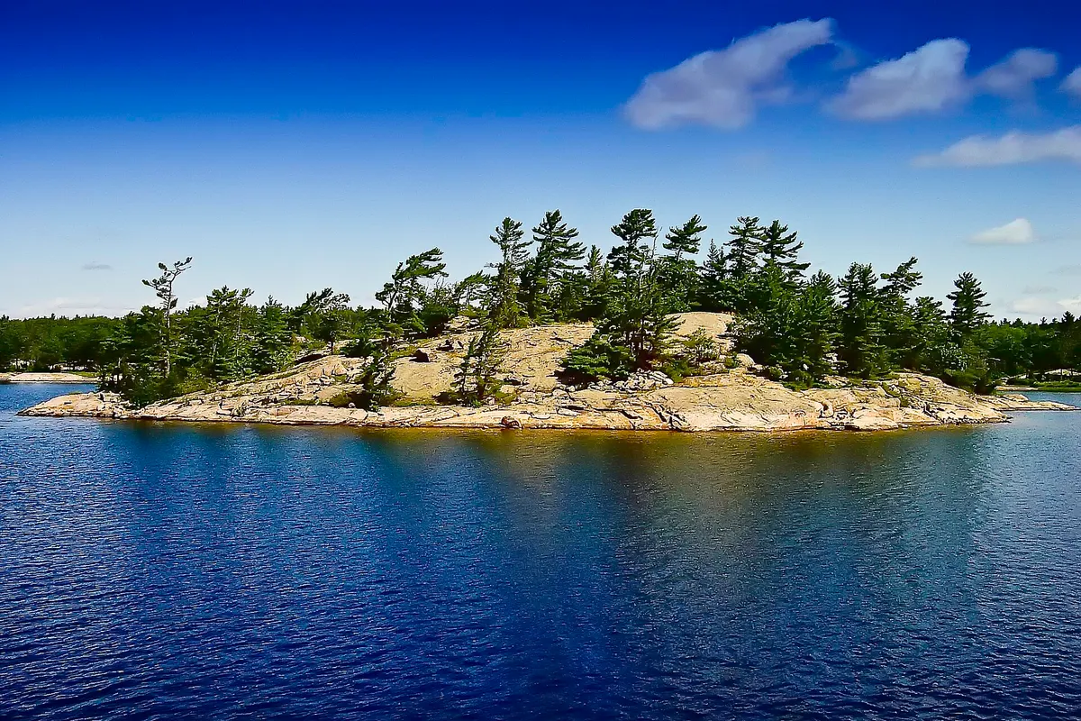 A small rocky island topped with pine trees on a blue lake in Ontario’s Muskoka region