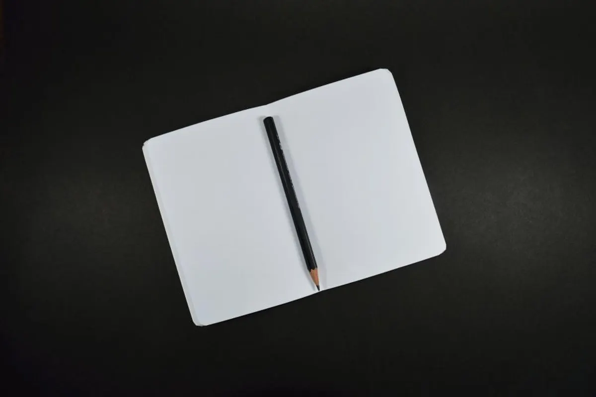 A pencil lying across an open blank notebook on a dark desk