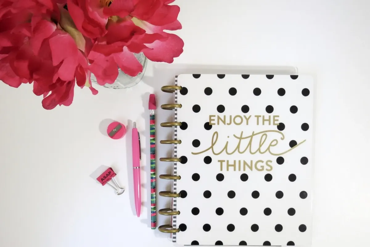 A spiral planner with a polka-dot cover beside pink pens and flowers