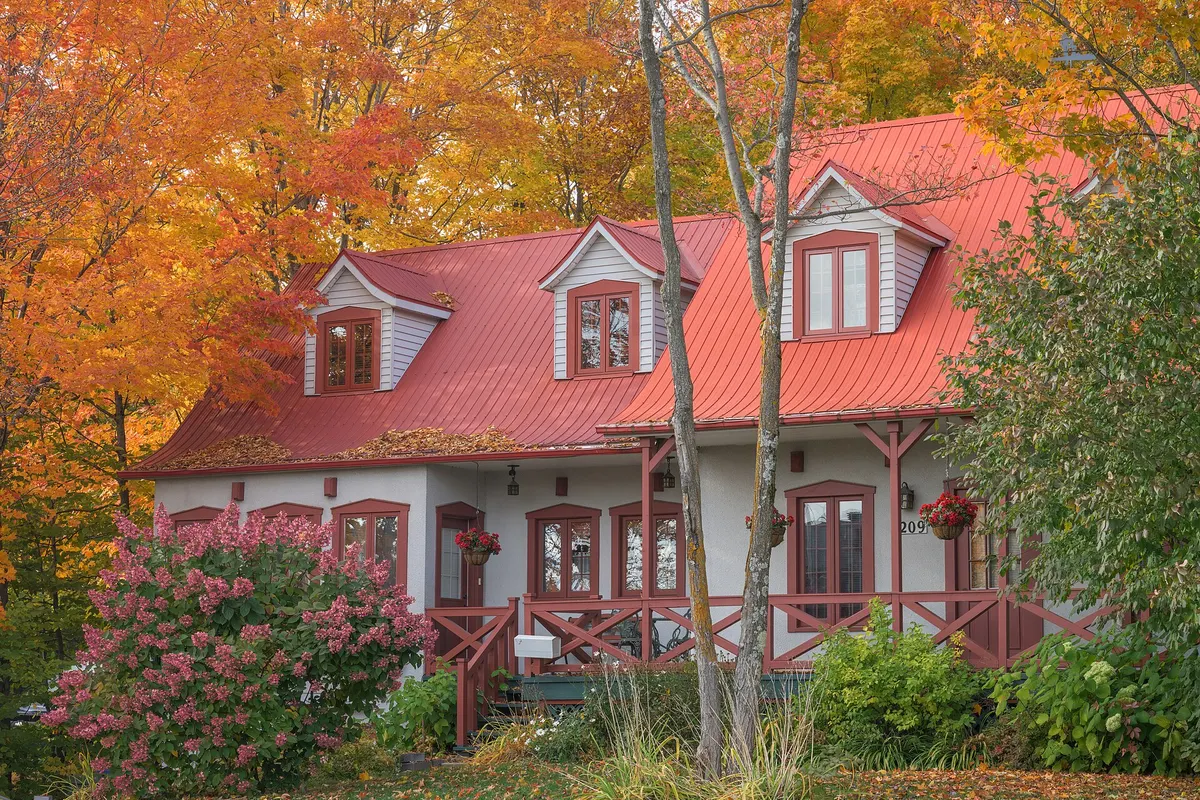 A red-roofed house in Quebec framed by orange and red autumn maples