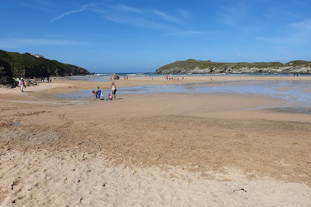 Families walking on a wide sandy beach in Cornwall at low tide under a blue sky