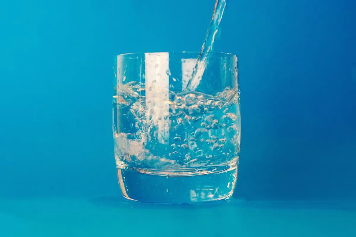 Water pouring into a clear glass against a bright blue background