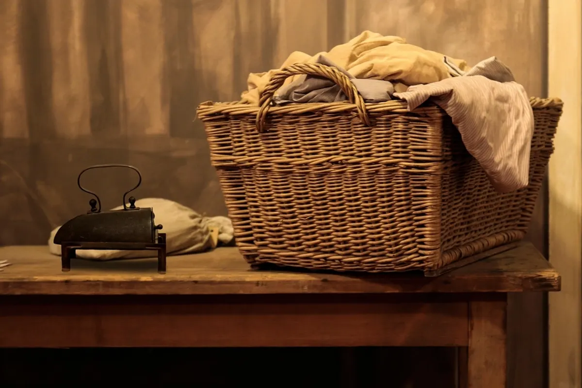 Wicker laundry basket piled with clean washing beside an old iron on a wooden table