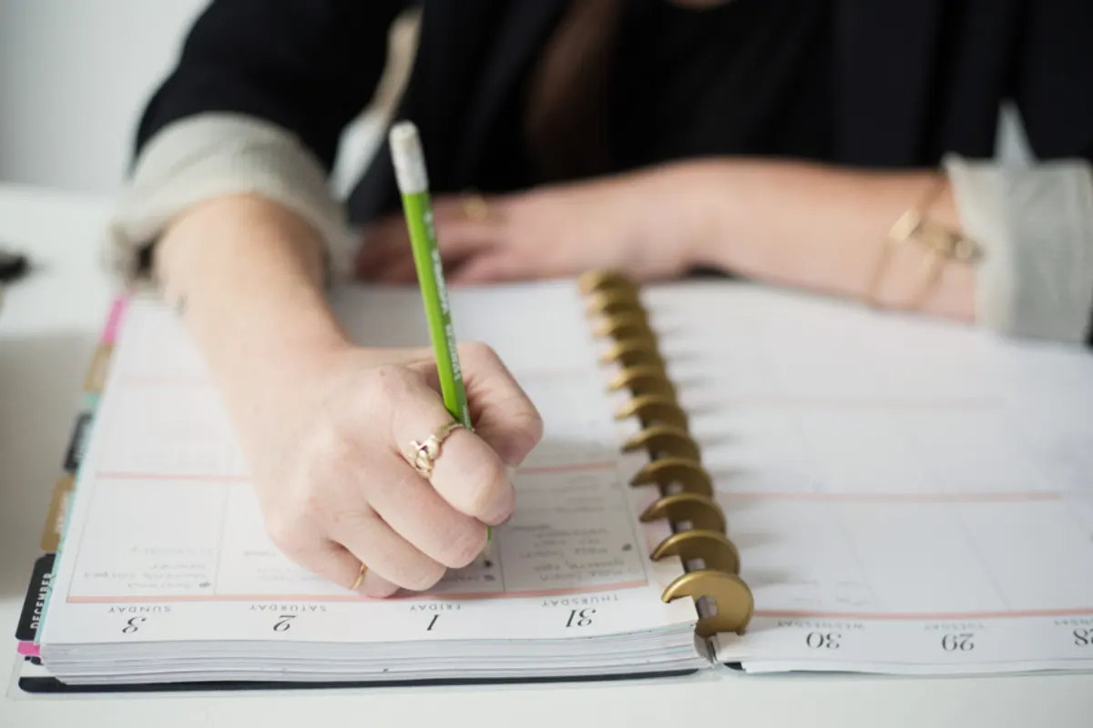 A hand writing dates into an open disc-bound planner with a green pencil